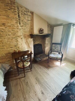 Une pièce avec un mur en pierre, une cheminée, une table en bois avec une chaise, et une chaise à motifs floraux.