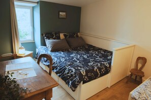 Ein Schlafzimmer mit Bett, einem Holztisch, einem Stuhl, einem Heizkörper und einem Fenster.