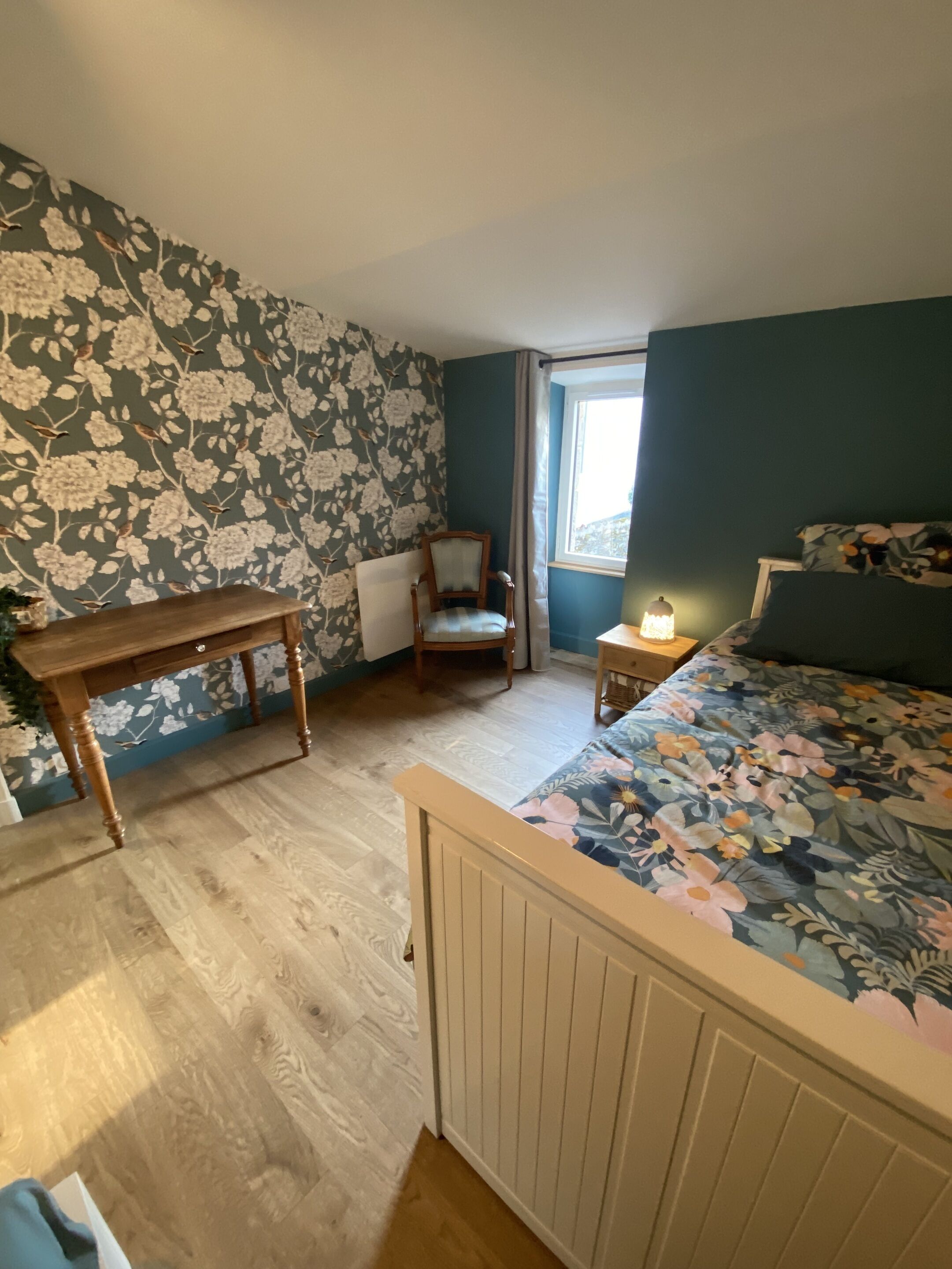 A bedroom with a wooden bed, a wooden nightstand, a chair, a table, and a window with curtains.