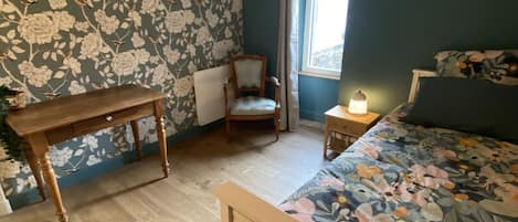 A bedroom with a wooden bed, a wooden nightstand, a chair, a table, and a window with curtains.