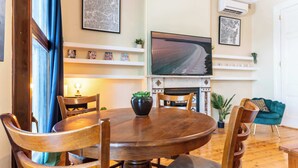 Un coin repas comprenant une table ronde en bois, des chaises, un téléviseur fixé au mur et une cheminée avec une étagère.