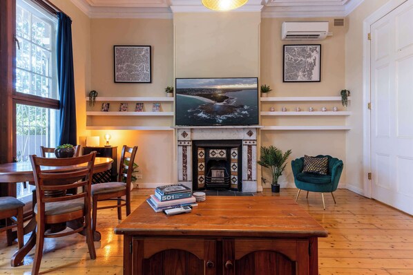 A cozy living room with a fireplace, a television mounted above it, and a dining area with wooden furniture. - Large and Stylish Petersham Apartment with Parking (Petersham)
