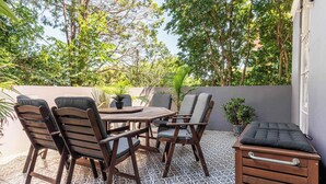Une terrasse avec une table et des chaises en bois, entourée de plantes en pot et d’un petit banc en bois.