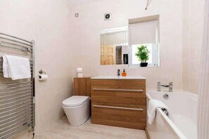 Ein Badezimmer mit Toilette, einem hölzernen Waschtisch mit Spiegel, einer Badewanne und einem Handtuchhalter.