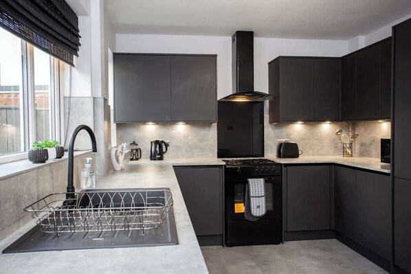 A modern kitchen with dark cabinetry, a stainless steel sink, a built-in oven, and a window with blinds.