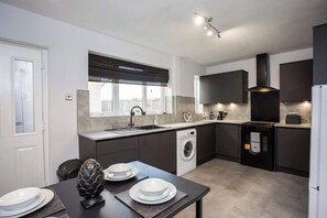 A modern kitchen with a built-in washing machine, a large window with blinds, and a flat-screen TV mounted above the counter.