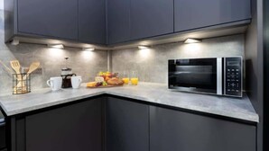 A modern kitchen with dark cabinets, a microwave, and a breakfast setup on the counter. - Vacant Nests | The Carrick  | Beach | Golf Course (Hartlepool)