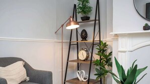 A living room with a grey sofa, a floor lamp, a bookshelf with plants, a clock, and a fireplace. - Vacant Nests | The Carrick  | Beach | Golf Course (Hartlepool)