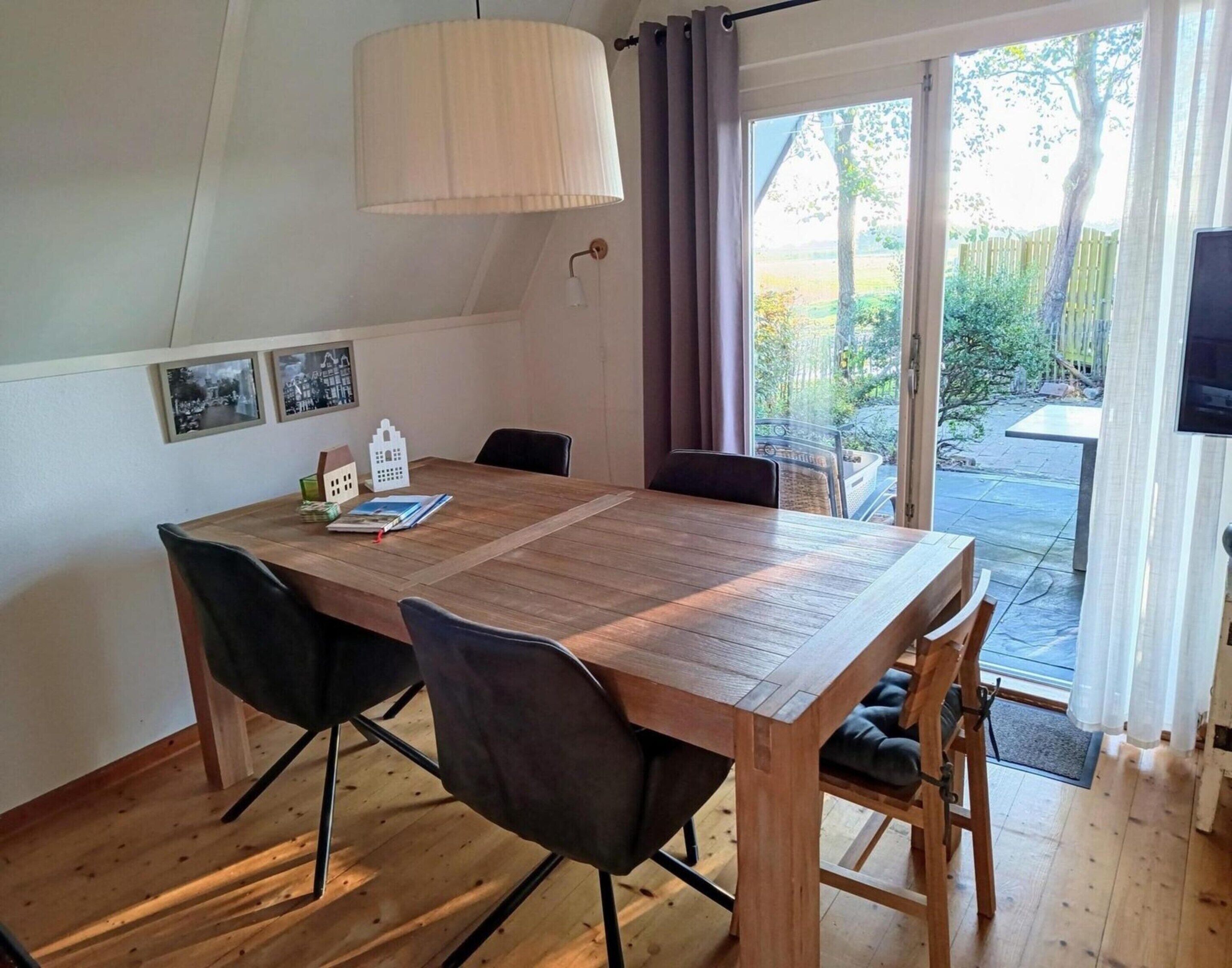 A dining area with a wooden table, black chairs, a hanging light fixture, and a view of the outdoors through a glass door.