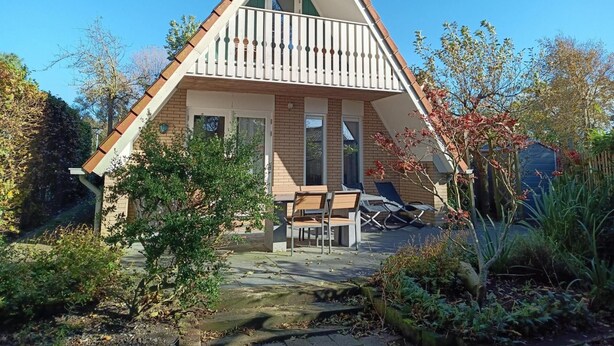 A triangular-roofed house with a balcony, a small garden, and outdoor seating. - Cozy Holiday Home in Sint Maartenszee (Sint Maartensvlotbrug)