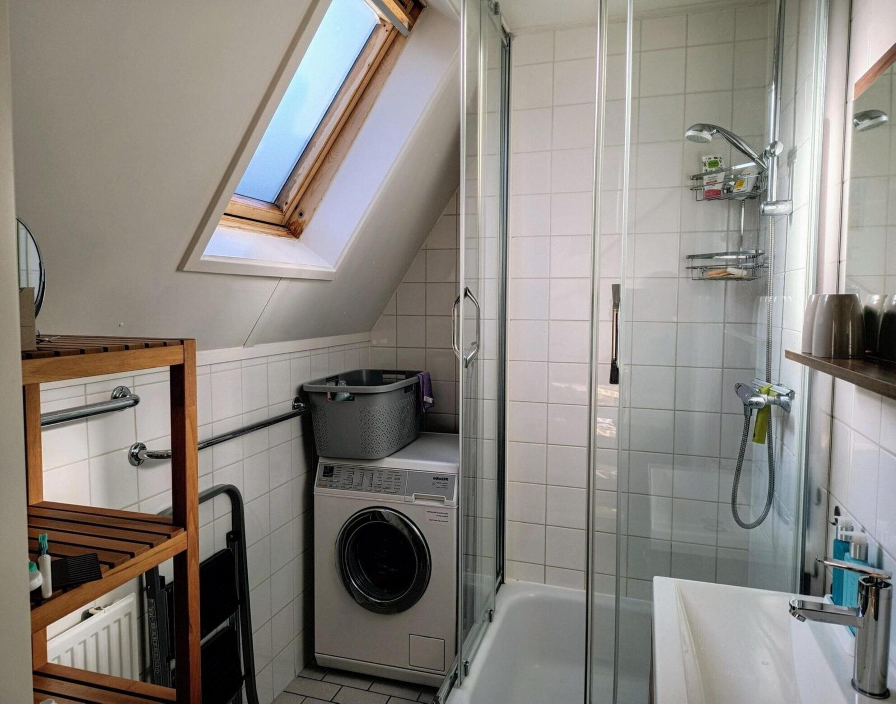 Une salle de bain compacte dotée d’un puits de lumière, d’un lave-linge, d’une douche à parois de verre et d’une baignoire.