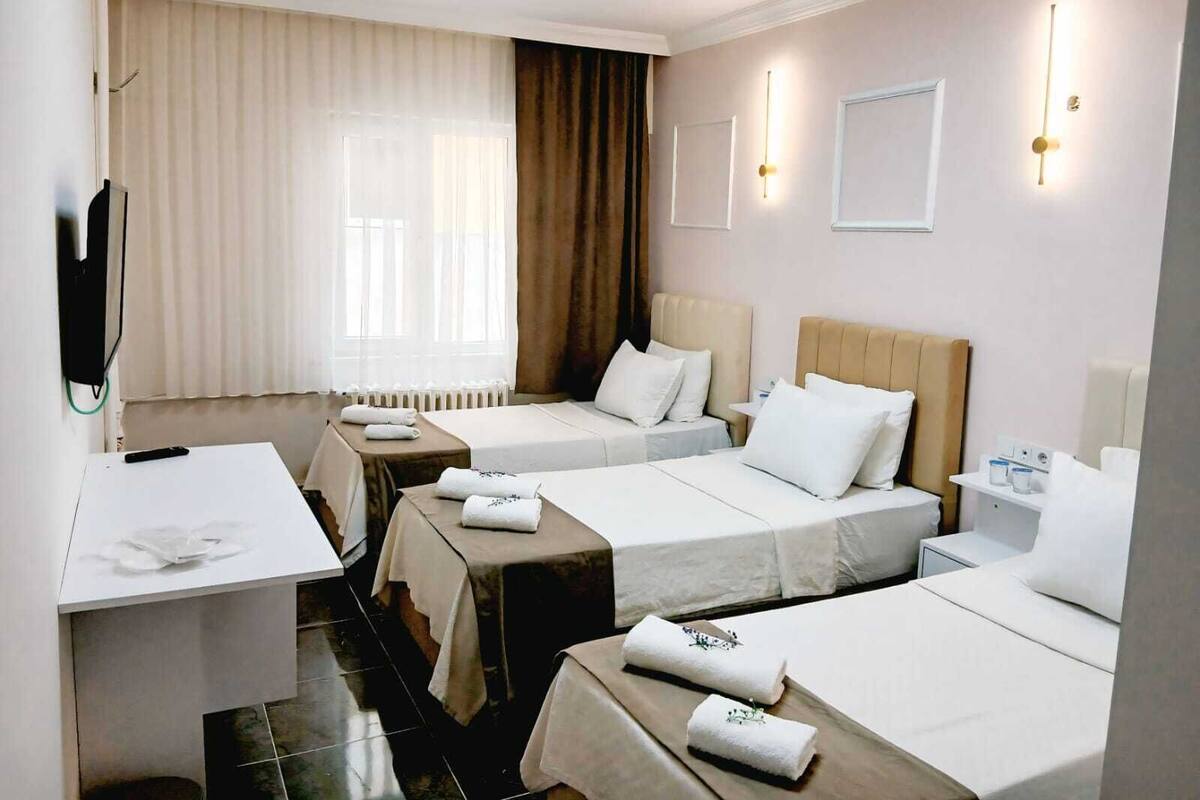 A hotel room with two beds, a desk, a TV, and a window with curtains.
