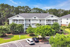 A multi-story hotel with a central courtyard, parking lot, and surrounding greenery. - Angie's Place w Huge Resort Pool n Hot Tub (North Myrtle Beach)