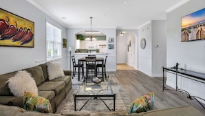 A modern living room with a glass coffee table, a sofa, and a dining area with chairs and a table. - Angie's Place w Huge Resort Pool n Hot Tub (North Myrtle Beach)