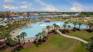 A large, irregularly shaped swimming pool surrounded by palm trees and lounge chairs, with a view of a marina and city skyline in the background. - Angie's Place w Huge Resort Pool n Hot Tub (North Myrtle Beach)