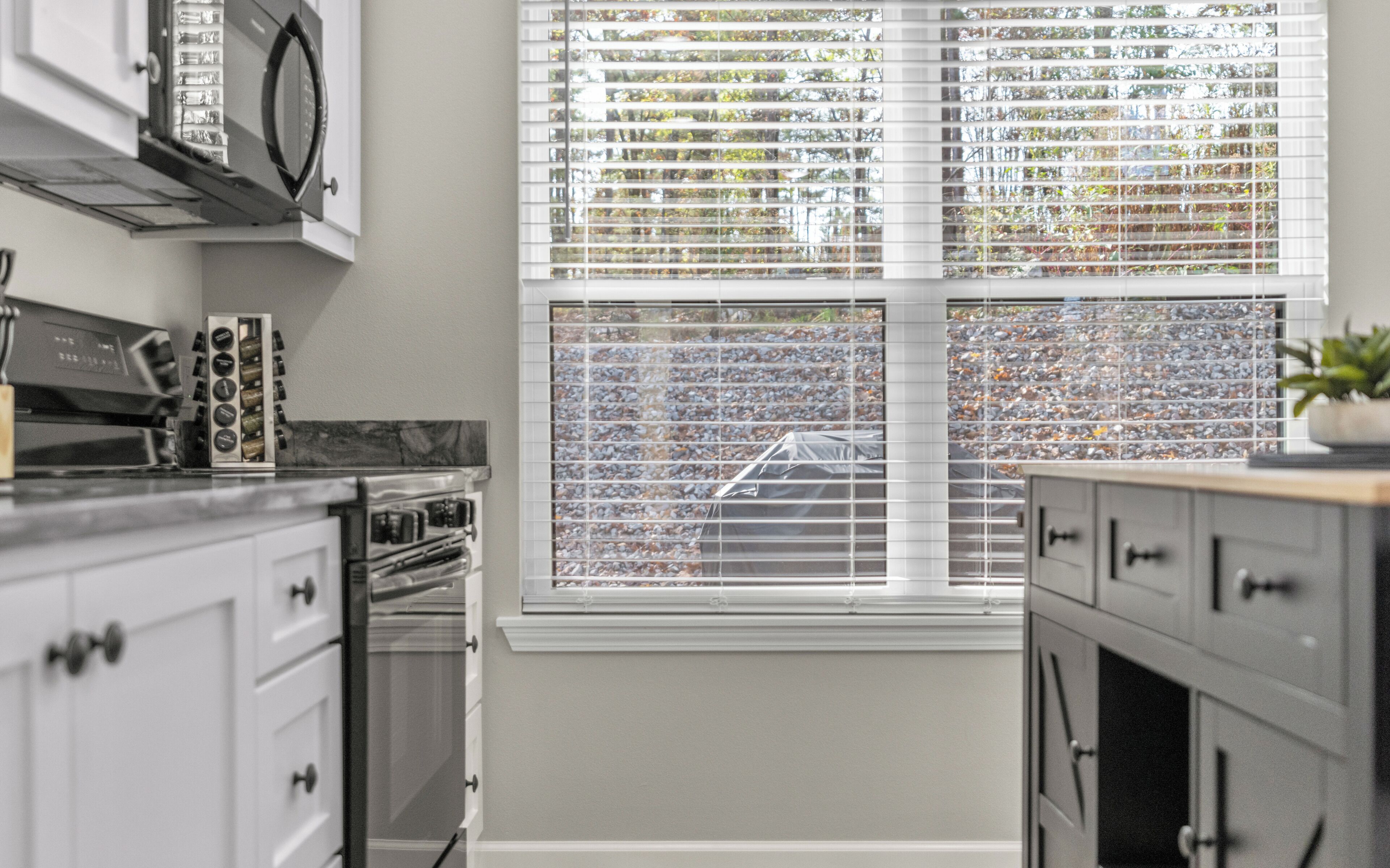 A kitchen with white cabinets, a built-in oven, and a window with decorative blinds.