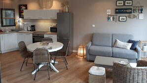 A modern kitchen with white cabinets, a grey refrigerator, and a dining area with wicker chairs and a round table.