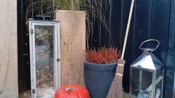 A wooden door, a large planter with red foliage, a pumpkin, a broom, and a lantern.