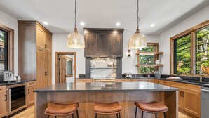 A spacious kitchen with a large island, wooden cabinets, and pendant lighting. - The Tree House | Exclusive Tamarack Perks (Tamarack)