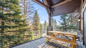 A wooden deck with a picnic table and a stone wall, overlooking a forested area. - The Tree House | Exclusive Tamarack Perks (Tamarack)