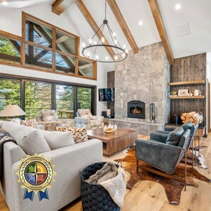 A spacious living room with a stone fireplace, wooden beams, and a large window overlooking greenery.