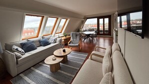 Ein modernes Loft-Apartment mit Schlafpodest, einer Couch, einem Esstisch und Blick auf die Stadt durch große Fenster.