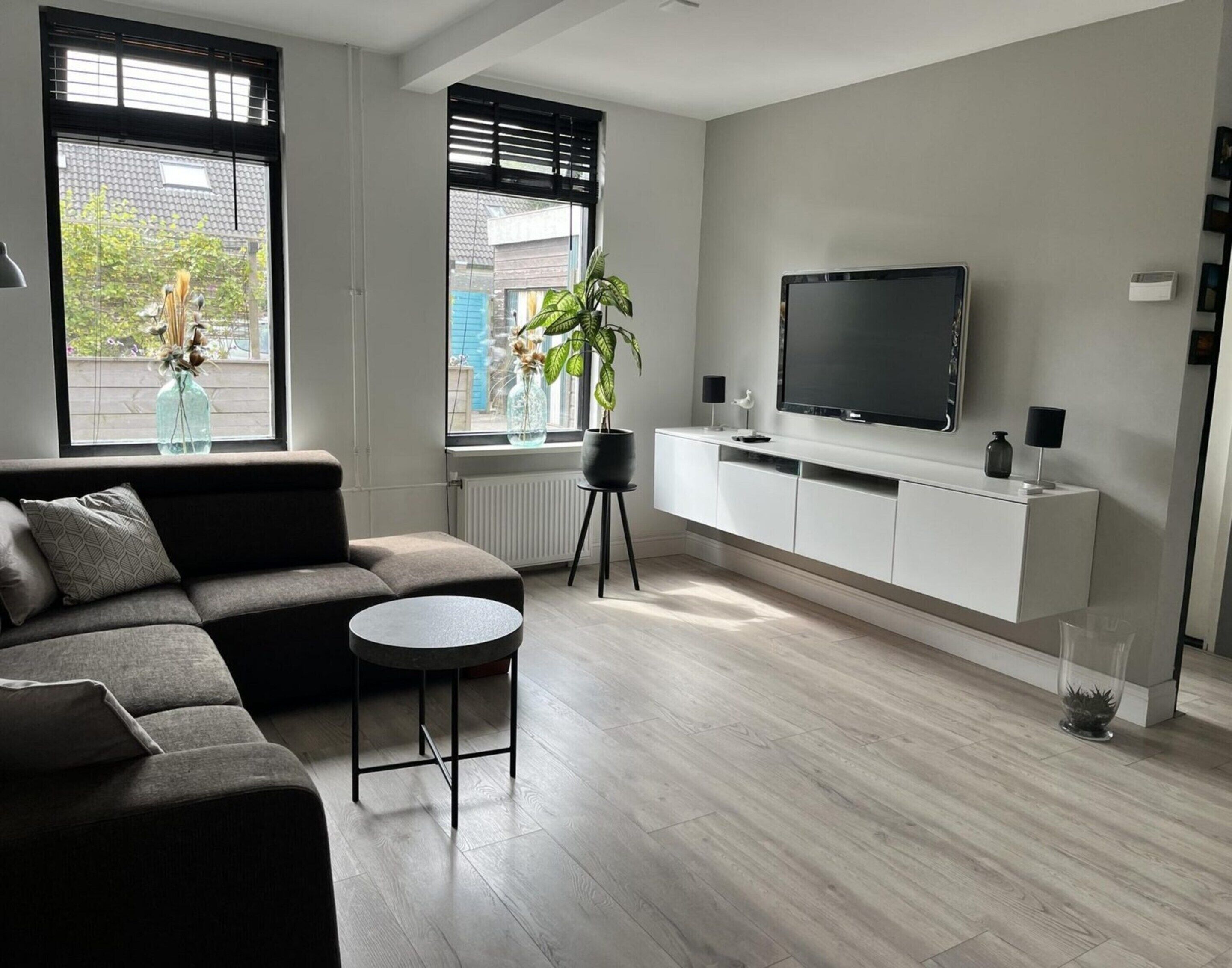 Een moderne woonkamer met een modulaire bank, een ronde salontafel, een televisie op een wit meubelstuk en een potplant.