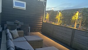 An outdoor patio with wicker furniture, a wooden deck, and a view of trees and flowers. - Holiday Home Near Dunes, Beach, sea (Sint Maartensvlotbrug)
