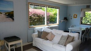 A living room with a white sofa, a small table, and a window with a view of greenery. - Attractive Bungalow Near Beach, Dunes (Sint Maartensvlotbrug)