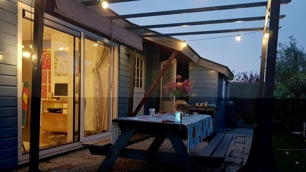 An outdoor patio area with a table and chairs, a wooden deck, and string lights. - Attractive Bungalow Near Beach, Dunes (Sint Maartensvlotbrug)
