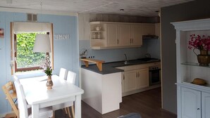 A compact kitchen with white cabinetry, a small island, and a dining area with a table and chairs. - Attractive Bungalow Near Beach, Dunes (Sint Maartensvlotbrug)
