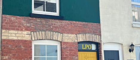 A two-story building with a green facade, a yellow door labeled "LPO", and a brick lower section.
