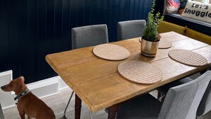A dining area with a wooden table, grey chairs, a blue wall clock, and a potted plant. - Dog Friendly Brixham Cottage, 3 Minutes to Harbour (Brixham)