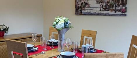 Une table à manger dressée avec des assiettes, des verres et des couverts, un vase rempli de fleurs et une nappe rouge.