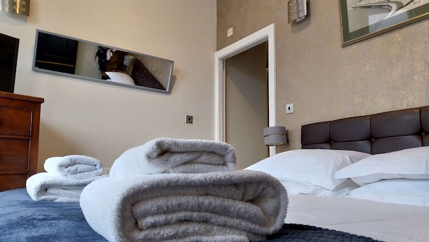 A hotel room with a bed, a dark blue blanket, and neatly folded towels.