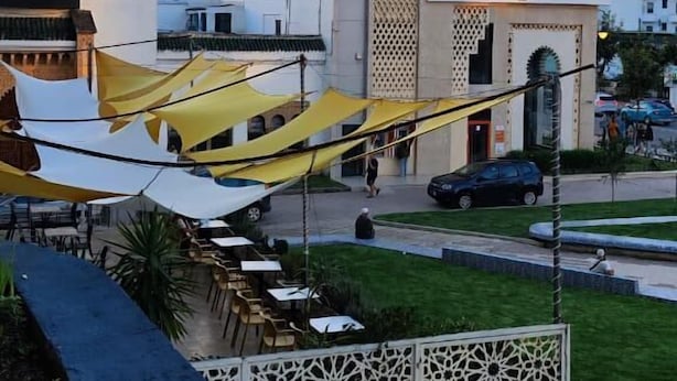 A view of a mosque with a tall minaret, a modern building with a sign, and a street with cars and pedestrians. - apartment ibiria (Tangier)