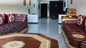 A spacious living room with a high ceiling and decorative molding, featuring a central coffee table and two sofas with patterned upholstery. - apartment ibiria (Tangier)