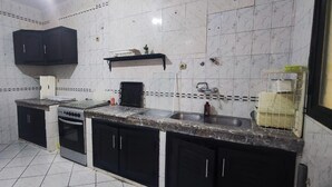 A compact kitchen with a white refrigerator, black cabinets, a stove, and a sink. - apartment ibiria (Tangier)