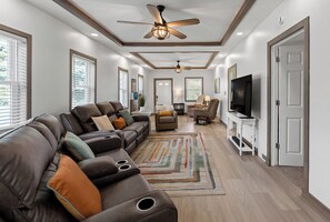A modern living room with a sectional sofa, a TV, and a ceiling fan. - Downtown Fun Meets Ultimate Game Night (Muskegon)