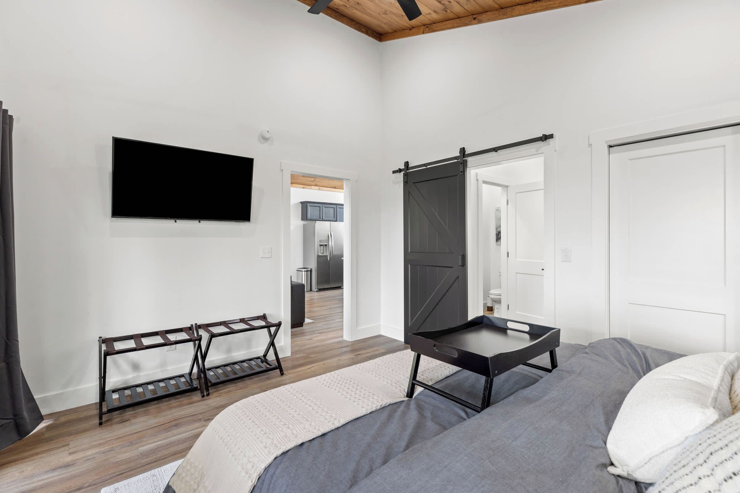 Un dormitorio con una cama, un televisor montado en la pared, una puerta corredera y vistas a la cocina.