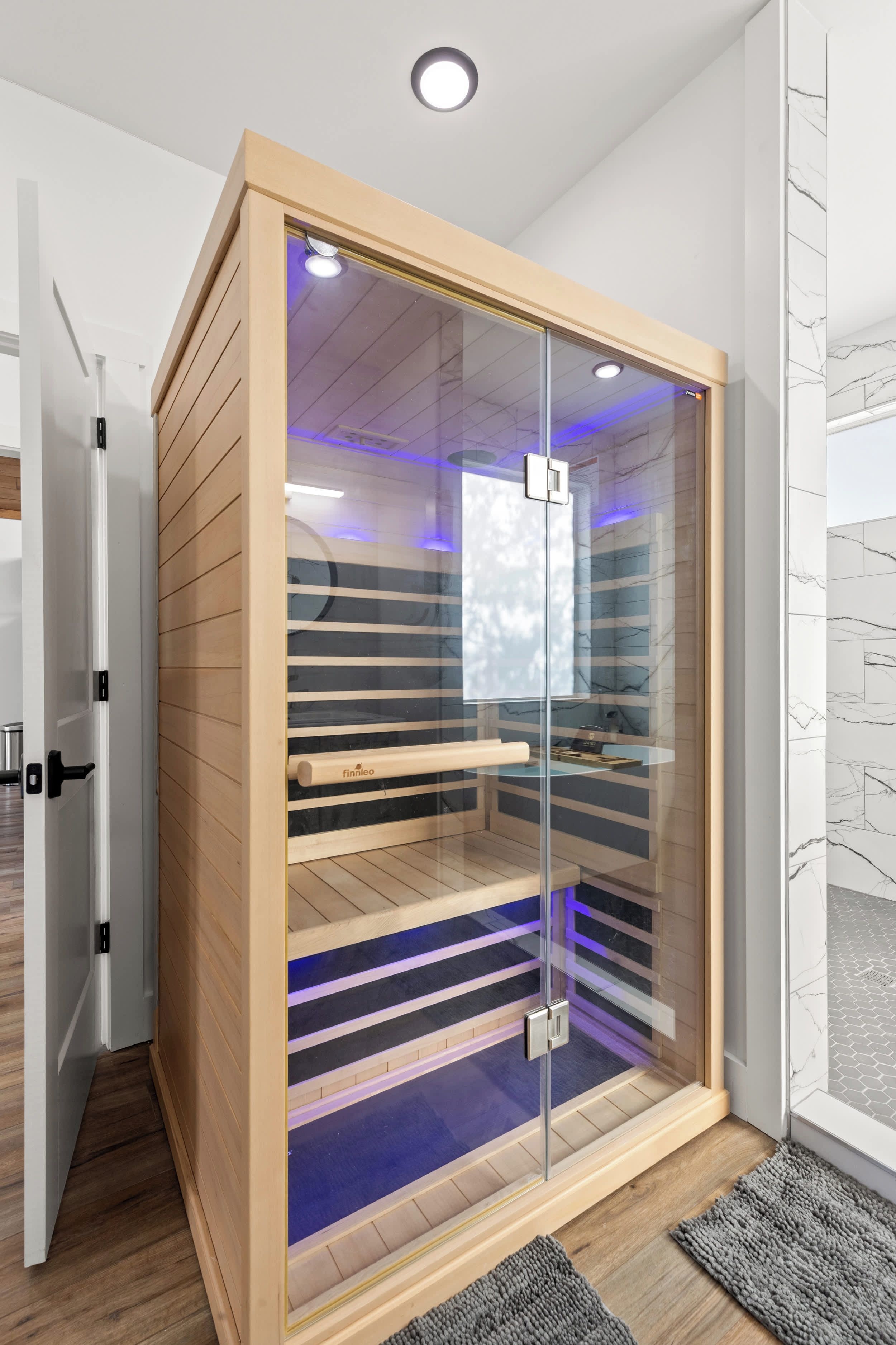 A modern sauna with a glass enclosure, wooden slats, and a control panel.