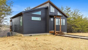 Une maison moderne à deux étages, dotée de grandes fenêtres et d’une terrasse en bois.