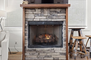 Una chimenea de piedra con fuego, un sofá blanco y un taburete de madera.