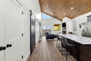 Een moderne keuken met een houten plafond, een bar met krukken, en een grote koelkast.
