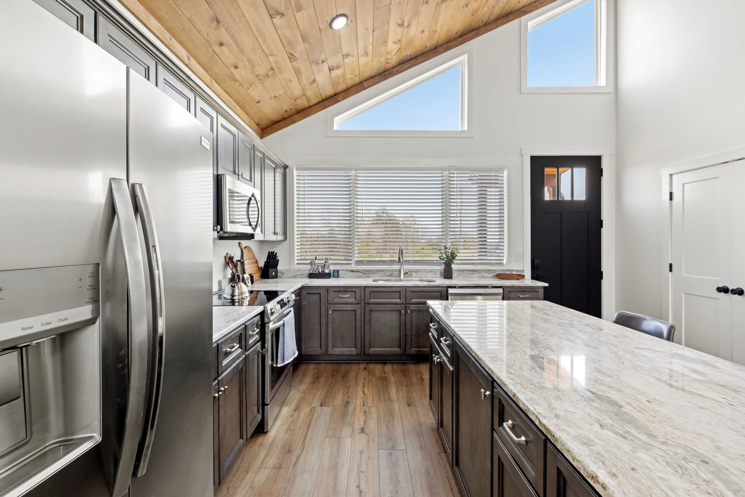 A modern kitchen with a stainless steel refrigerator, wooden cabinets, a marble countertop, and a skylight.