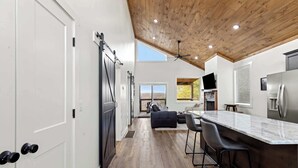 Une cuisine moderne avec un plafond en bois, un coin bar avec des tabourets et un grand réfrigérateur.