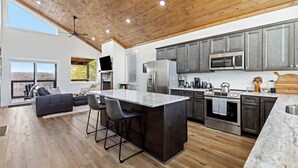 Une cuisine moderne dotée d’un grand îlot central, d’appareils électroménagers en acier inoxydable et d’un plafond en bois.