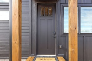 Una puerta principal de madera oscura con un pequeño ventanal arriba, un felpudo con la palabra “Welcome” y un timbre.