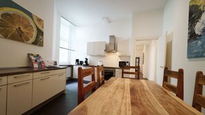 A modern kitchen with white cabinets, a wooden dining table, and a large window providing natural light.