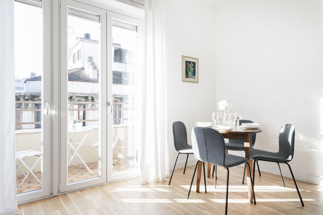 Un coin repas avec une table dressée pour quatre personnes, une porte-fenêtre coulissante donnant sur un balcon extérieur et un tableau encadré accroché au mur.